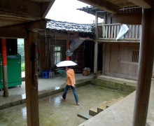 A person with an umbrella walking through the open courtyard in a traditional yard house.