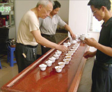 Three men standing around a long wooden table lined with many gaiwans and cups to taste and compare the rock wulong.