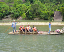 A raft with a handful of passengers, being poled along the river by two people.