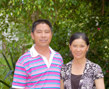 A smiling couple standing in front of green trees.