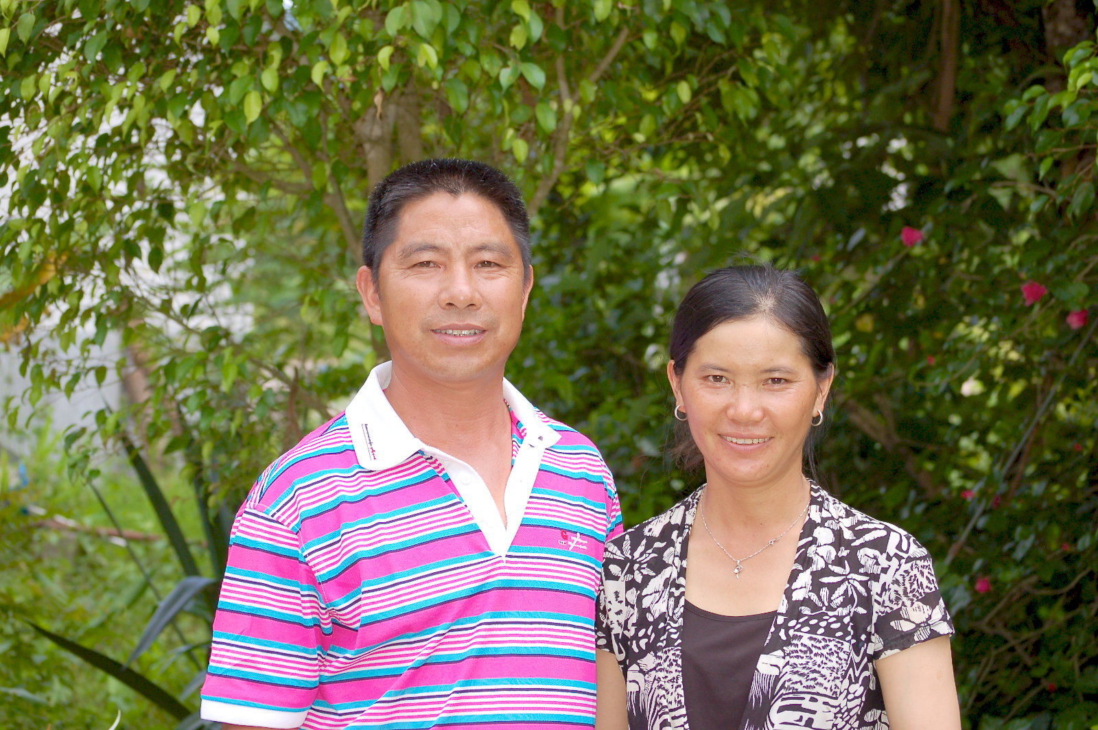 A smiling couple standing in front of green tea trees.