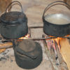 Two pots and a kettle boiling over a fire inside a village home.