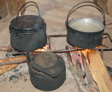 Two pots and a kettle boiling over a fire inside a village home.