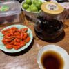A plate of goji berries next to a class pot of a dark shu puer.