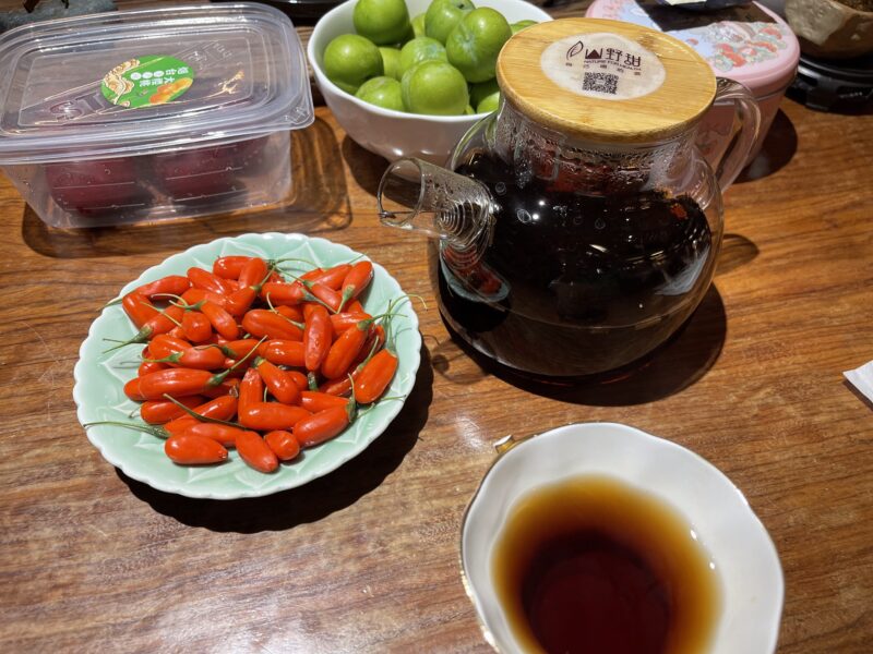 A plate of goji berries next to a class pot of a dark shu puer.