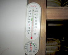 A thermometer showing the temperature and humidity in a room holding finished puer cakes.