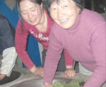 Two women frying Mogan Huangya tea by hand in a wok