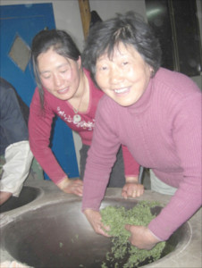 Two women frying Mogan Huangya tea by hand in a wok