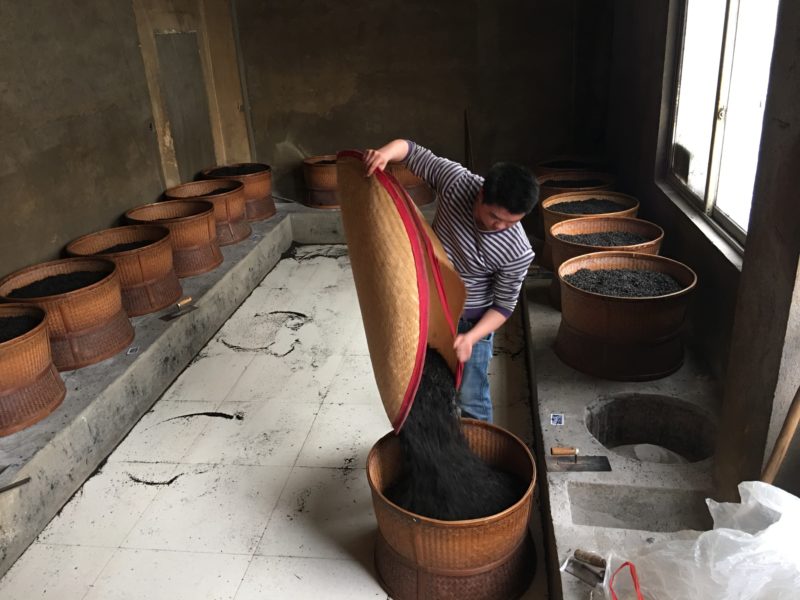 Roasting Rock Wulong tea in traditional "Bei Long" baskets over coals. The worker regularly agitates the leaves to distribute heat.