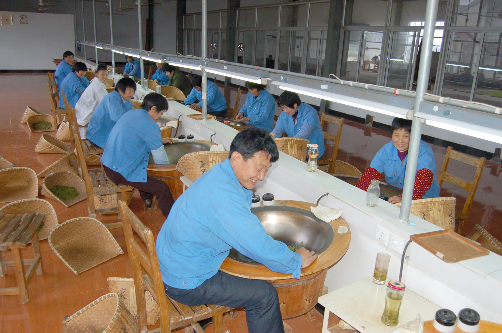 A row of workers frying Da Fo Longjing tea leaves by hand in their woks.
