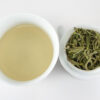 Cupped infusion of Mengding Ganlu (Sweet Dew) green tea and strained leaves.