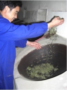 The tea maker takes up the tea gently in his hands and shakes the buds into the rims of the wok.