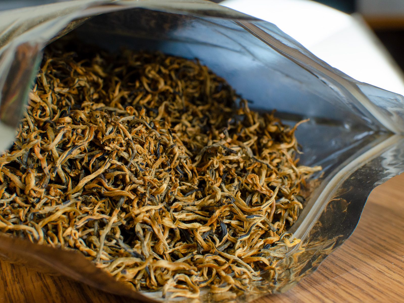A package of freshly opened Jinya (Yunnan Golden Buds) black tea with the dry leaves spilling out of the silvery zipper bag.