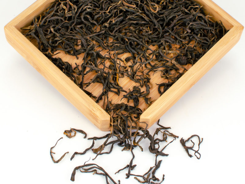 Jin Konque (Golden Peacock) dry black tea leaves displayed on a bamboo tray.