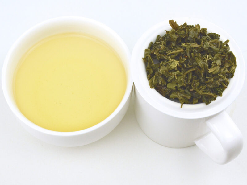 Cupped infusion of Buddha's Eyebrow (Fo Mei) green tea and strained leaves.