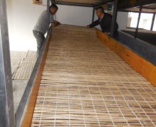 Two people unrolling a long bamboo mat to lay in the upper part of the wind tunnel.