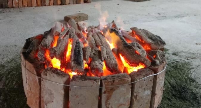 A blazing open-flame circular charcoal brazier used for roasting Lu'an Gua Pian.