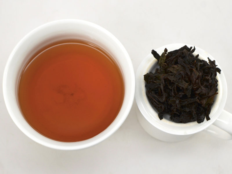 Cupped infusion of Da Hong Pao (Big Red Robe) rock wulong tea and strained leaves.