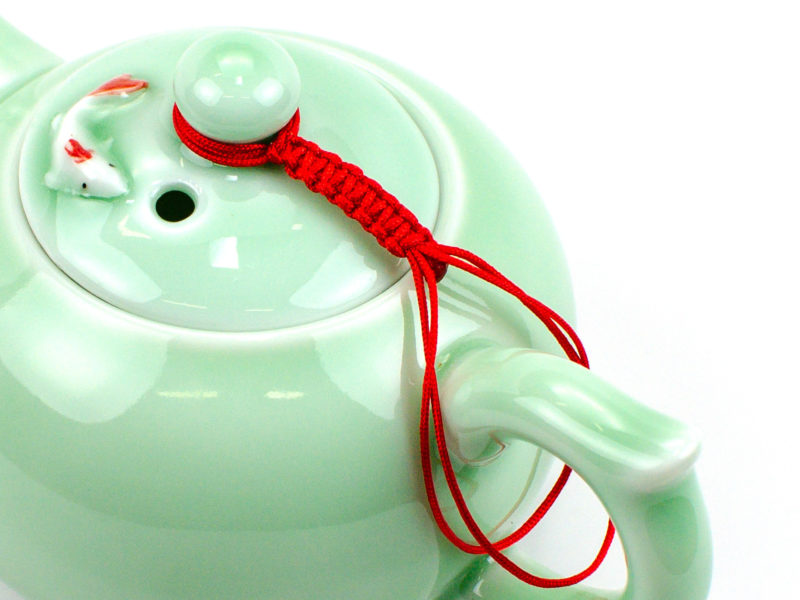 A braided red cord connecting a teapot's lid to its handle.