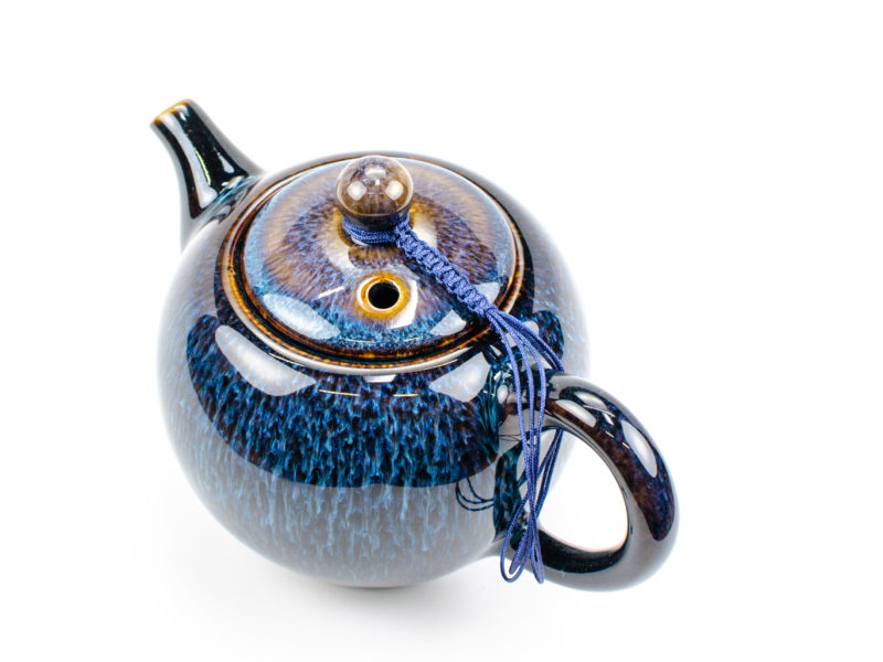 A braided blue cord connecting a porcelain teapot's lid to its handle.