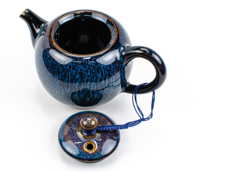 A braided blue cord connecting a porcelain teapot's lid to its handle even when open.