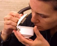 A woman evaluating tea aroma by smelling a gaiwan full of tea.