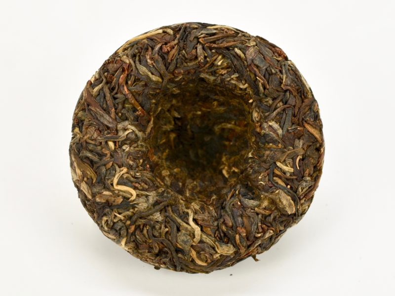 A round Little Sheng Tuocha 2014 Sheng Puer Cake unwrapped to show the compressed tea leaves in shades of dark green and the deep indentation in the center of the back of the puer cake.