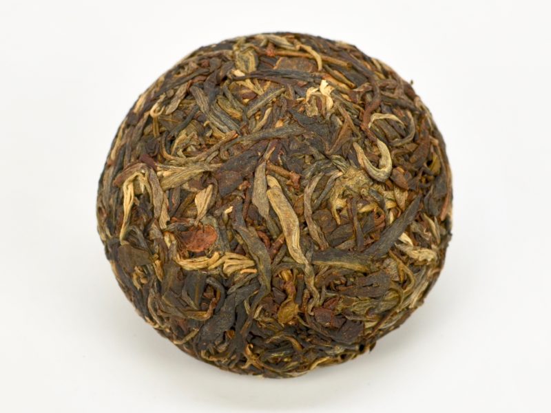 A round Little Sheng Tuocha 2014 Sheng Puer Cake unwrapped to reveal the compressed tea leaves in shades of dark green.