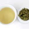Cupped infusion of Da Fo Longjing (Big Buddha Dragon Well) green tea and strained leaves.
