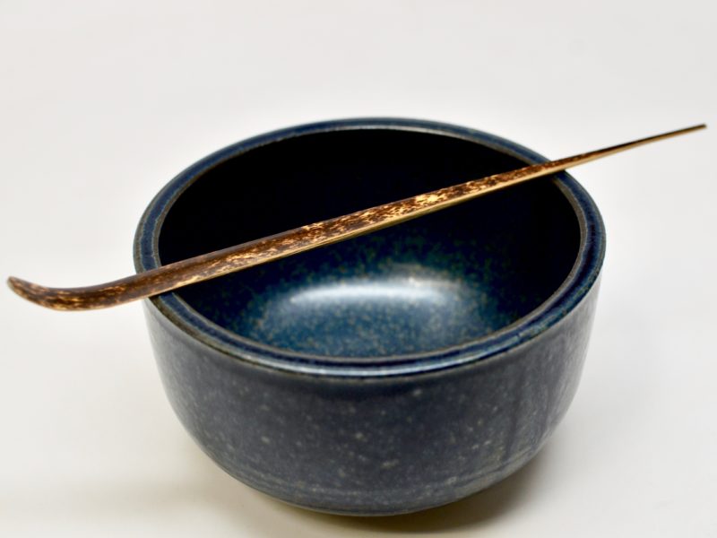 A purple bamboo matcha scoop resting on top of a matcha bowl.