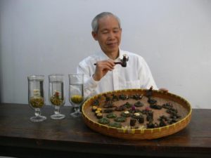 Display tea inventor Wang Fang sheng sitting in front of a tray filled with several types of display tea.