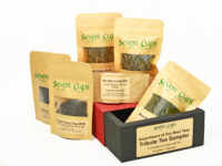Small bags of the six teas included in the Tribute Tea Sampler arranged around and of top of its decorative cardboard box.
