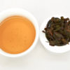 Cupped infusion of Traditional Tieguanyin Anxi wulong tea and strained leaves.