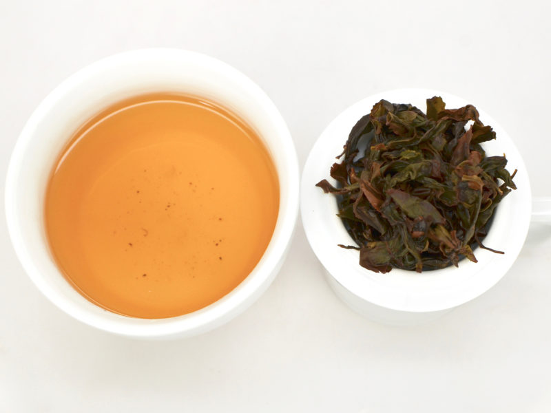 Cupped infusion of Traditional Tieguanyin Anxi wulong tea and strained leaves.