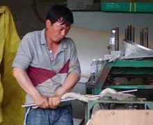 A man operating a machine to compact a wrapped ball of tea.