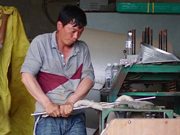A man operating a machine to compact a wrapped ball of tea.