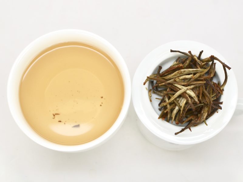 Bai Long Xu (White Dragon Whiskers) wet tea leaves next to a cup of the infused tea