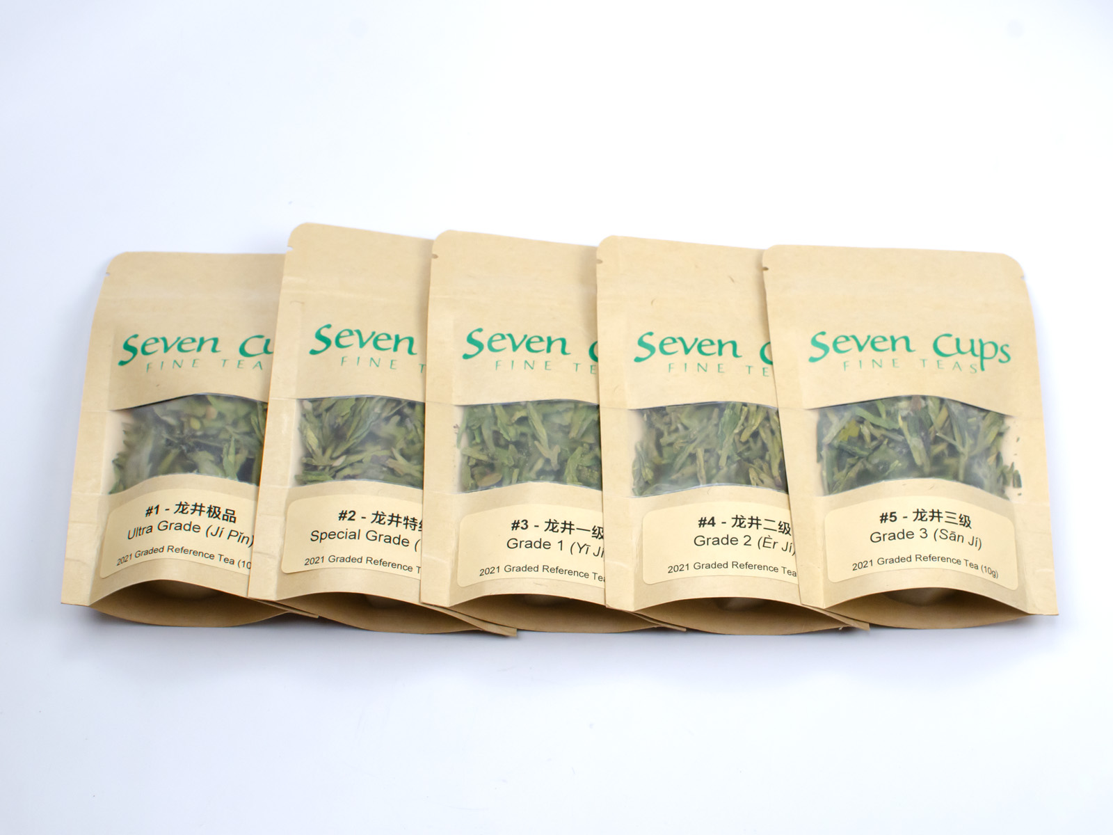 Small bags of the five Longjing teas included in the Dragon Well sampler, spread out in a straight line.