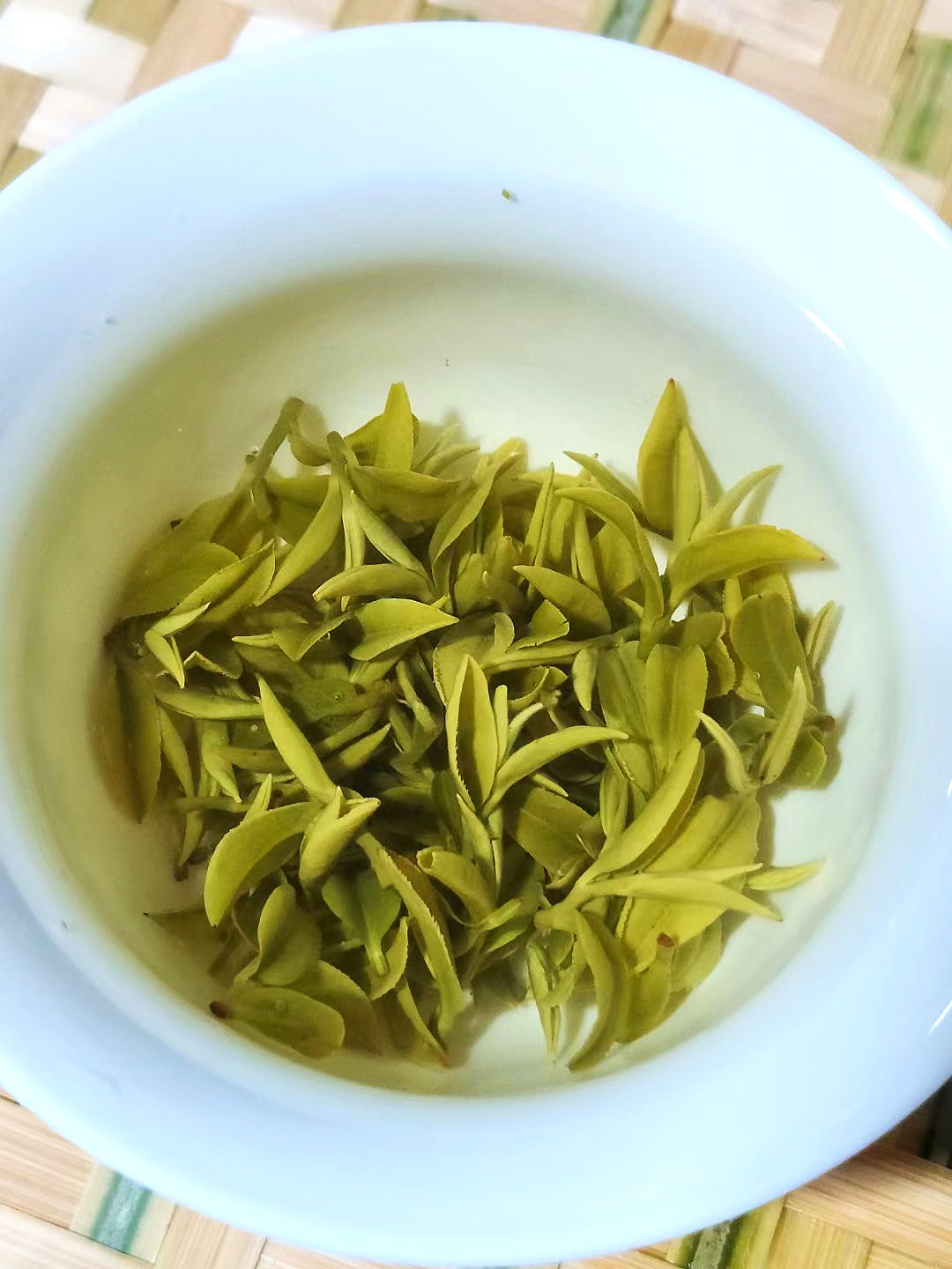 Looking down into a gaiwan brewing very crisp, clean and even green tea leaves with a delicate pale infusion.