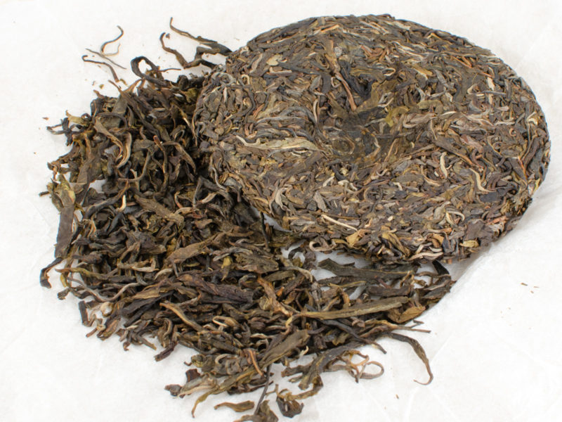 Xiaohuzhai 2019 sheng puer cake on open wrapper with broken out tea leaves placed beside cake.
