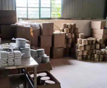 A storeroom with several stacks of freshly wrapped puer cakes on a table and several bamboo-wrapped tongs of stacked cakes in the background.