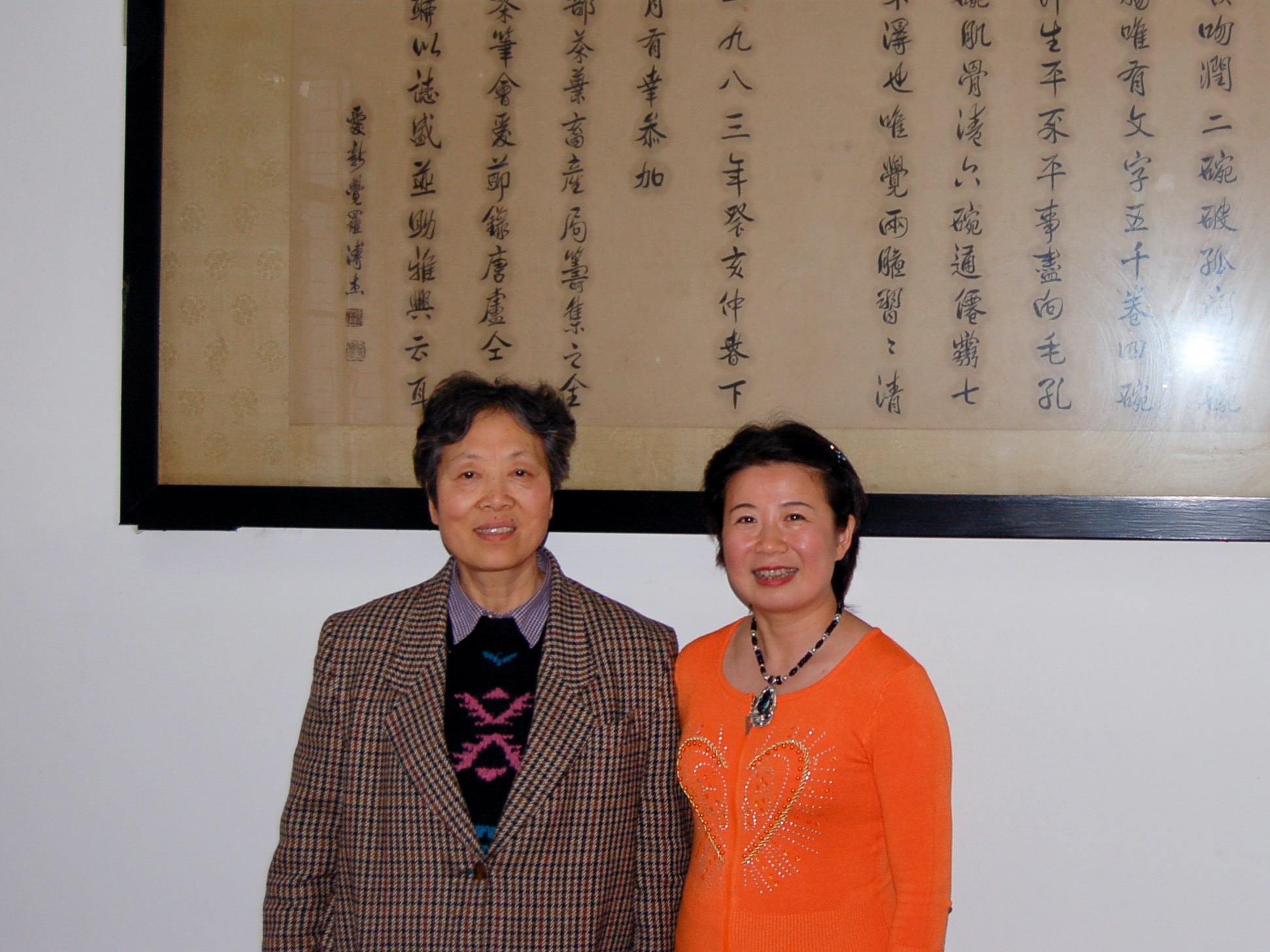 Two people standing in front of a large piece of framed calligraphic art, smiling.
