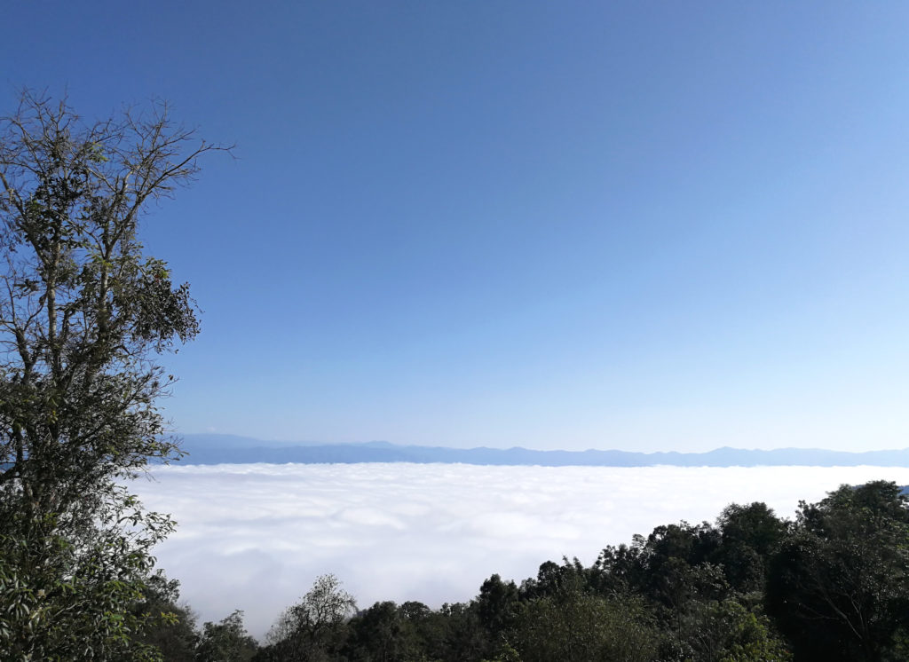 Looking down from one of Jingmaishan's mountain peaks to see a spectacular layer of clouds surrounding it below, with more mountains springing up from it in the far distance.