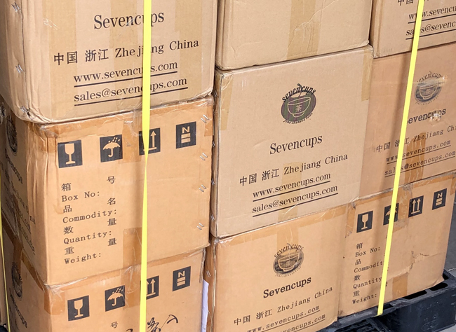 Stacked cardboard shipping boxes of tea with the Seven Cups company logo on the side, lashed to a pallet. 2020.