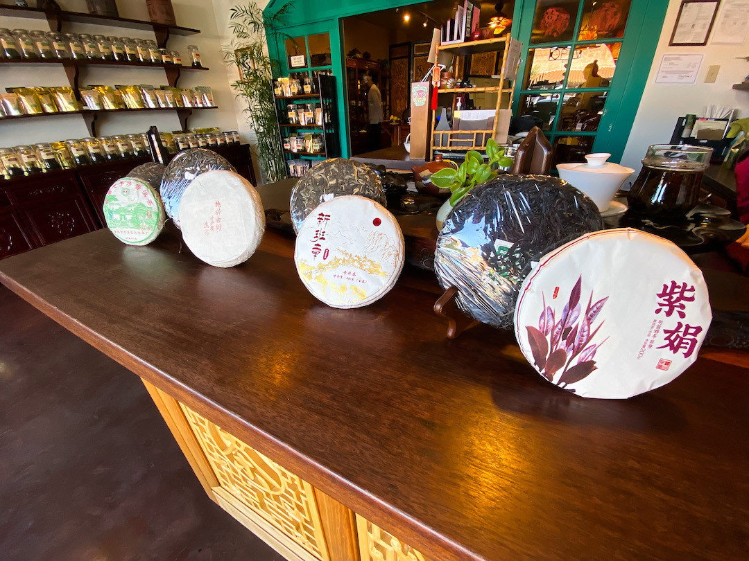 Four puer cakes on stands laid out on the heavy wooden counter of the tea table at the front of the tea shop.