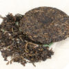 Jingmaishan (Jingmai Mountain) 2007 sheng puer cake on open wrapper with broken out tea leaves placed beside cake.