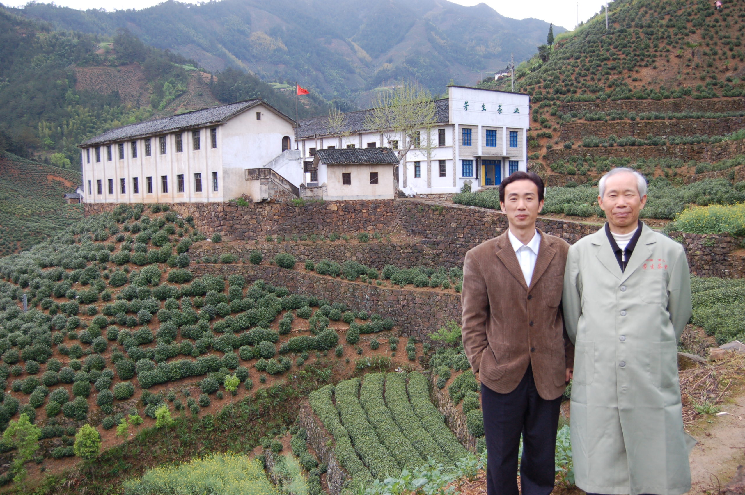 Wang Fangsheng (right) and Wang Huizhou (left), 5th and 6th generation tea makers, stand in front of their unique mountainside tea factory. This picture is from 2006, the first time Austin met them.