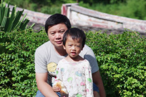 A man kneeling behind his young daughter in the garden.