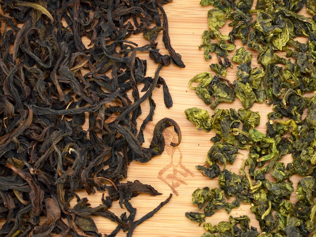 Close view of two dry wulong teas, one with long dark twisted leaves and one with compact green ones.