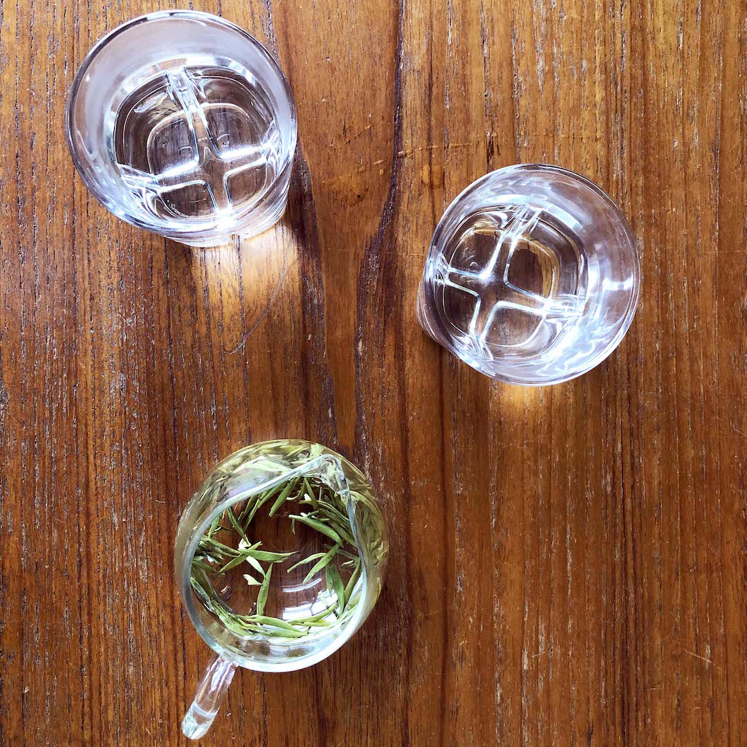 ea buds float in a glass pitcher next to two tumbler glasses atop polished wood grain of a table.